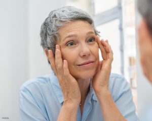 Older Women With Short Grey Hair Looking in the Mirror Examining her Eye Wrinkles Older Women With Short Grey Hair Looking in the Mirror Examining her Eye Wrinkles